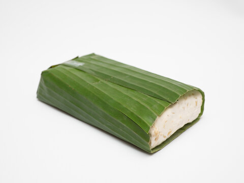 Block of tempeh or tempe, a traditional Indonesian food made from whole soybeans that are fermented and pressed into a dense, firm cake, with banana leaf wrapping in a white background