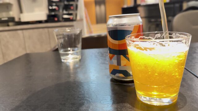 Pouring fresh craft beer into glass on dark table with colorful can in background.