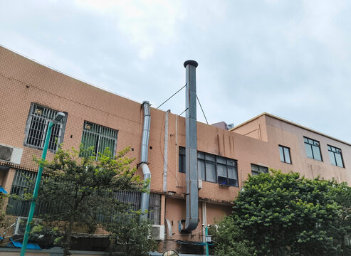 Outdoor galvanized steel fume ventilation pipe for commercial food shop kitchen, installed on building exterior wall. Unmaintained grease buildup inside this kind of duct easily causes fire risks.