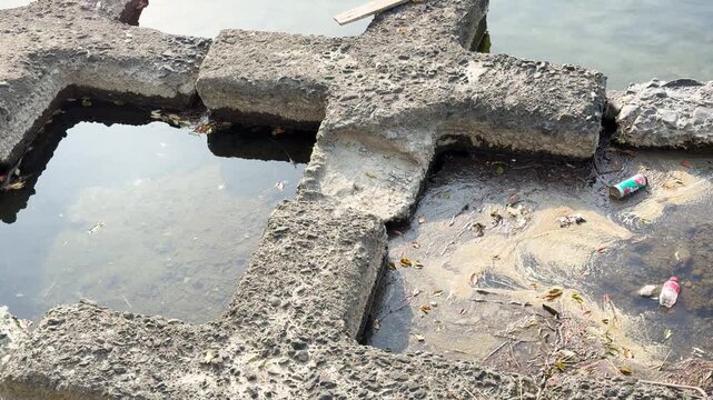 Floating debris and trash trapped in concrete wave breakers on a lake shore footage.