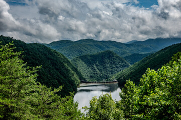 Distant view of a mountain valley reservoir and dam under a dynamic cloudy sky North Carolina