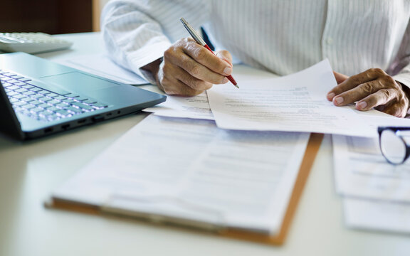 close up shot, asian businessman reviewing document at office working on laptop. professional lawyer reading and checking business documents and contract before giving advice to customers