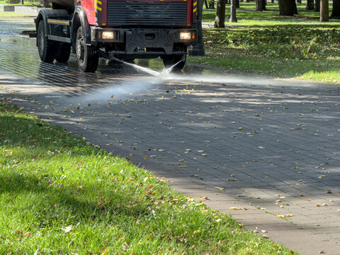 sprinkler truck washes the city park road with water spray. street flusher machine