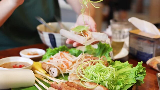 Woman hands using chopsticks to prepare traditional vietnamese spring roll with grilled pork and fresh vegetables.