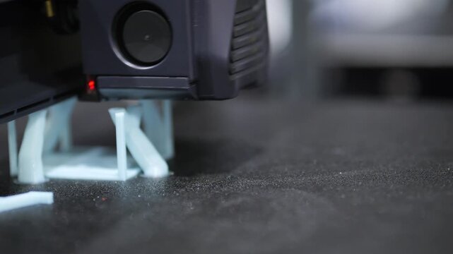 3D printer extrudes filament layer by layer. Machine builds plastic object slowly. Close-up shot of printing process in progress