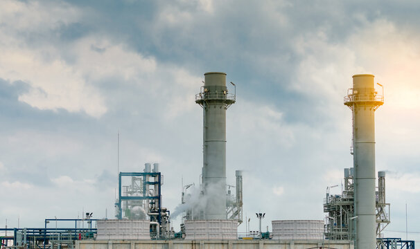 Natural gas power plant with industrial gas turbines, cooling towers and tall exhaust stacks generating electricity for factory operations beneath a dramatic cloudy sky. Reliable energy infrastructure