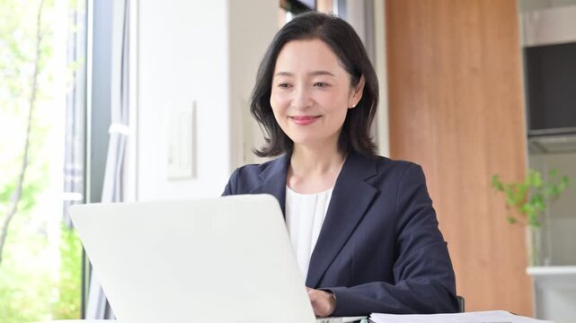 A video of a female office worker doing desk work on her laptop; a businesswoman working with a smile on her face in the office, resting her hand on her chin