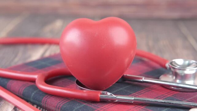 Red heart with medical stethoscope on a wooden table close up slow motion shot