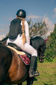 Equestrian rider on a dark horse wearing protective riding equipment outdoors