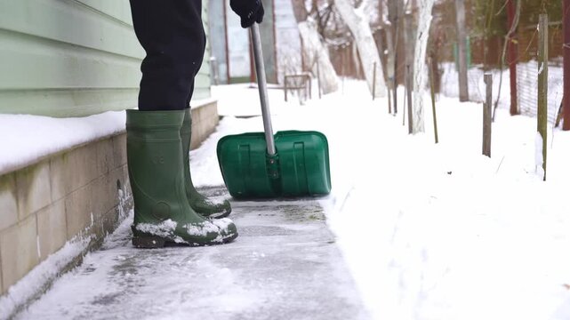 Man clears snow from outdoor yard using shovel during winter snowstorm, removing fresh snow from ground while heavy snowfall creates cold seasonal setting and active winter maintenance scene suitable