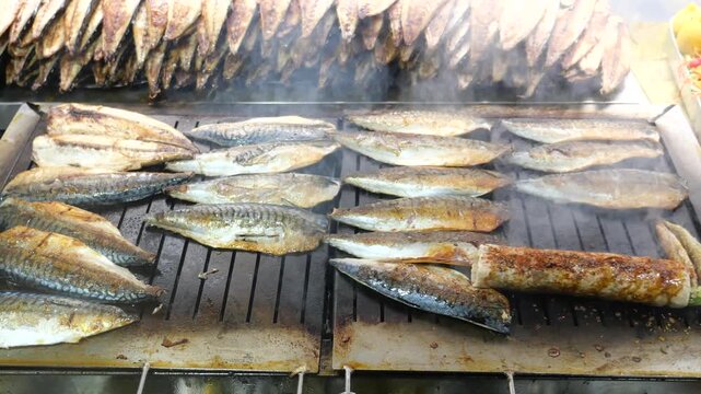 Chef grilling fresh mackerel fish fillets on outdoor charcoal grill at local street food market