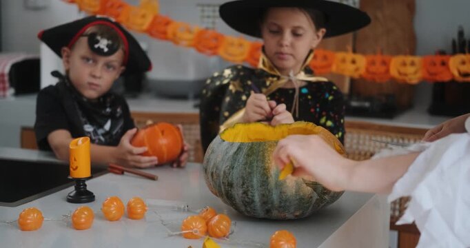 A portrait of a young girl and her younger brother celebrating Halloween and carving pumpkins in the kitchen with their mother's help. They are dressed in witch and pirate costumes. 