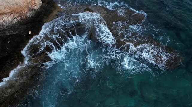 Drone aerial seascape Turbulent turquoise sea water waves breaking against a rugged and rocky shoreline from above