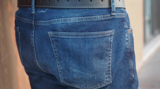 A close up cinematic shot of a person putting a black leather wallet in and out of the back pocket of blue jeans, illustrating financial security and everyday carry essentials