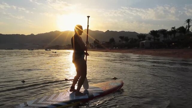 Young woman dancing on the sup board at sunset in Egypt