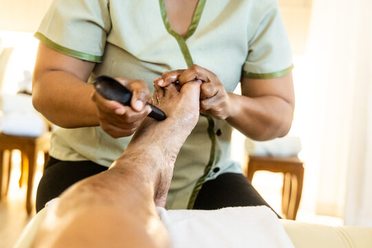 Close-up perspective view of masseuse using massage stick to perform traditional relaxing and therapeutic Thai foot and leg massage, pressing on all essential acupoints.