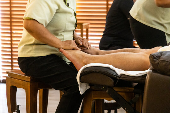 Close-up of masseuse performing traditional relaxing and therapeutic Thai foot and leg massage, pressing on all essential acupoints in nice ambient environment.