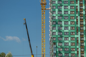 Construction of a towering building under a clear blue sky with a tall crane lifting materials to the upper floors © beholdereye
