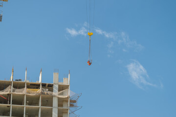 Construction crane lifting materials high above a building site under a clear blue sky filled with wispy clouds © beholdereye