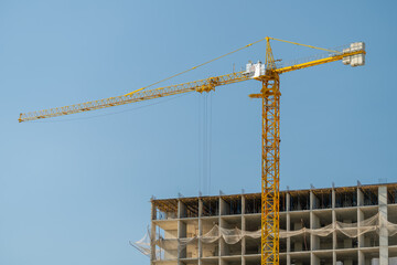Construction of a high-rise building unfolds under a bright blue sky with a towering crane actively lifting materials © beholdereye