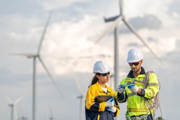 Fototapeta premium Teamwork engineers coaching wind turbine power generator sustainability performance brainstorming together at Renewable Energy Plant Male and female engineers reading compass inspecting windmill