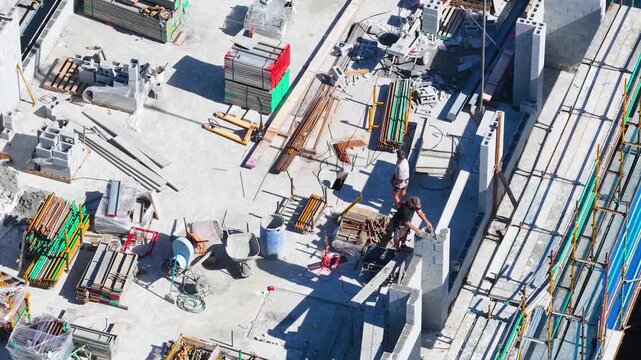 Aerial view of construction workers building high rise apartment using concrete blocks and steel reinforcement.
