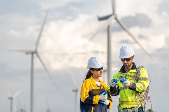 Teamwork engineers coaching wind turbine power generator sustainability performance brainstorming together at Renewable Energy Plant Male and female engineers reading compass inspecting windmill