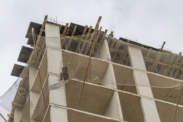 Construction of a modern building rises high against the cloudy sky in a bustling city area © beholdereye