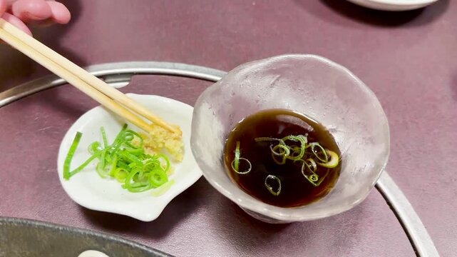 Dipping minced garlic and chopped scallions into soy sauce with chopsticks for seasoning food.