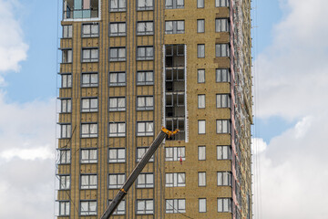 Construction work on a high-rise building under a cloudy sky as a crane lifts materials to the upper floors © beholdereye