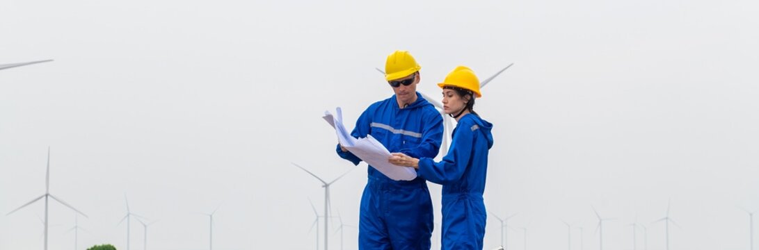Engineers Team inspecting wind turbine power generator sustainability performance inspection together at Renewable Energy Plant Male and female in coverall checking holding blueprints at windmill