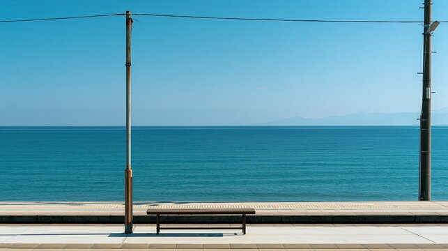 Serene seaside promenade with a lone bench facing the calm ocean under a clear blue sky