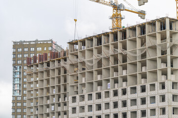 Construction progresses on a modern high-rise building amidst gray skies in a bustling urban area © beholdereye