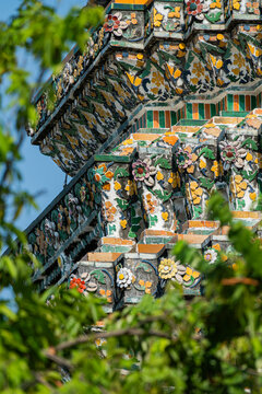 Porcelain mosaic flowers detail on Wat Arun prang framed by leaves