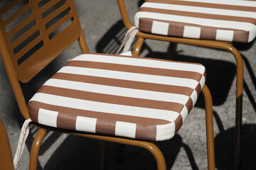 Obraz premium Striped cushions on metal chairs outdoors in a sunny setting