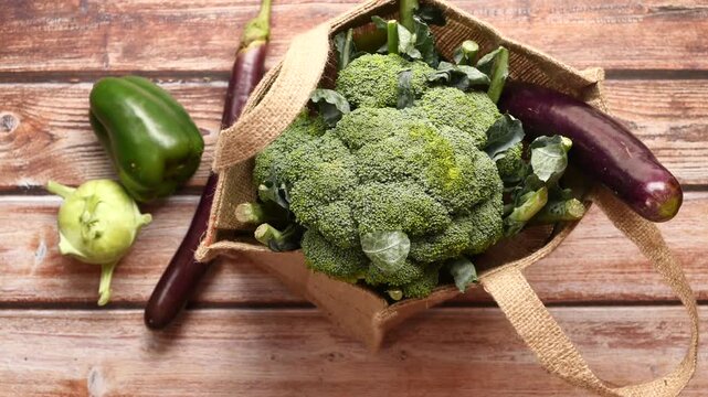 Top down view of fresh green organic broccoli in hessian shopping bag with other vegetables on wooden table