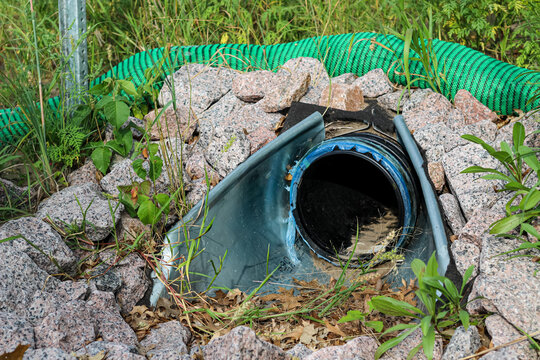 drainage culvert outlet with a black corrugated pipe set inside a flared end section, surrounded by protective landscaping rock.