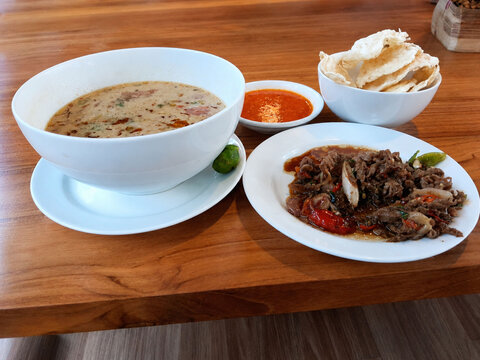 Soto Betawi is a traditional Indonesian dish featuring flavorful slices of beef cooked with chili and aromatic spices, served with a touch of sambal and crispy emping crackers. 