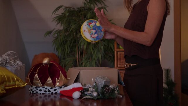 Woman dancing and playing a tambourine as if singing along to a Christmas carol while unpacking holiday decorations