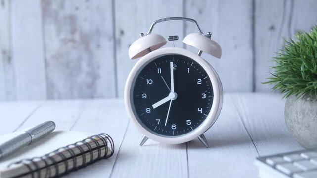 Alarm clock showing time passing by on desk with notebook and pen close-up footage