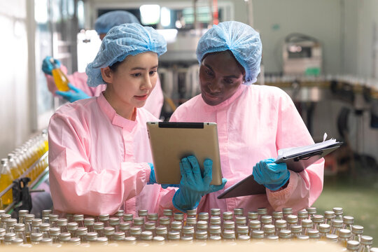 Asian and black factory worker inspect line product with tablet in beverage factory. Food and drinks Industry workers. 