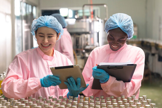 Asian and black factory worker inspect line product with tablet in beverage factory. Food and drinks Industry workers. 