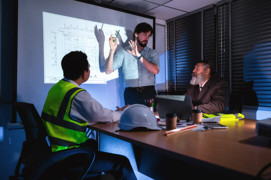 Engineering presenting and discuss floor plans on projector screen during late-night company meeting with senior project manager. Concept of brainstorming in construction project management with team.