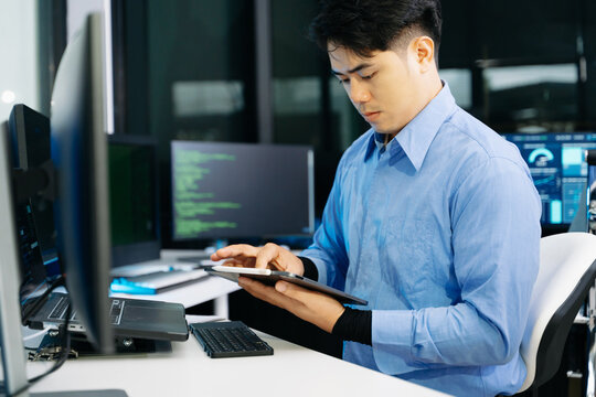 Asian developer writing code at night in modern office setup. Concept of software engineering, programming