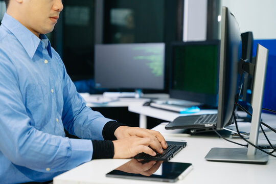 Asian developer writing code at night in modern office setup. Concept of software engineering, programming