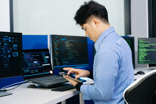 Asian developer writing code at night in modern office setup. Concept of software engineering, programming