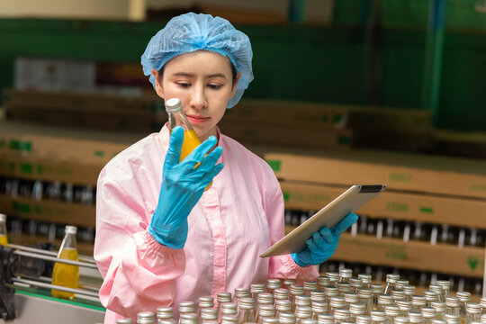 Asian female scientist working on tablet computer check quality of drinking beverage on conveyer belt before distribution to market.