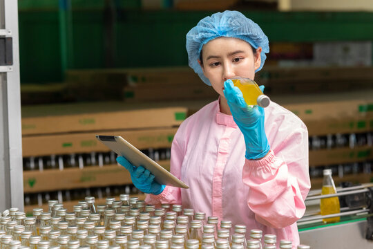 Asian female scientist working on tablet computer check quality of drinking beverage on conveyer belt before distribution to market.