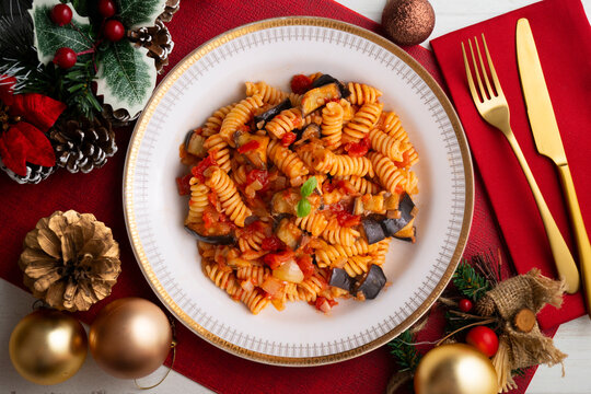 Delicious pasta alla Norma with eggplant and tomatoes. Traditional Italian recipe. Overhead shot. Christmas meal with festive decorations.