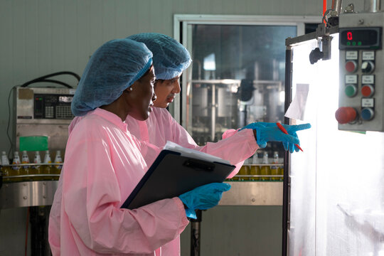 Asian male and black woman factory workers monitoring cold drink bottles on production line at drinks production plant.